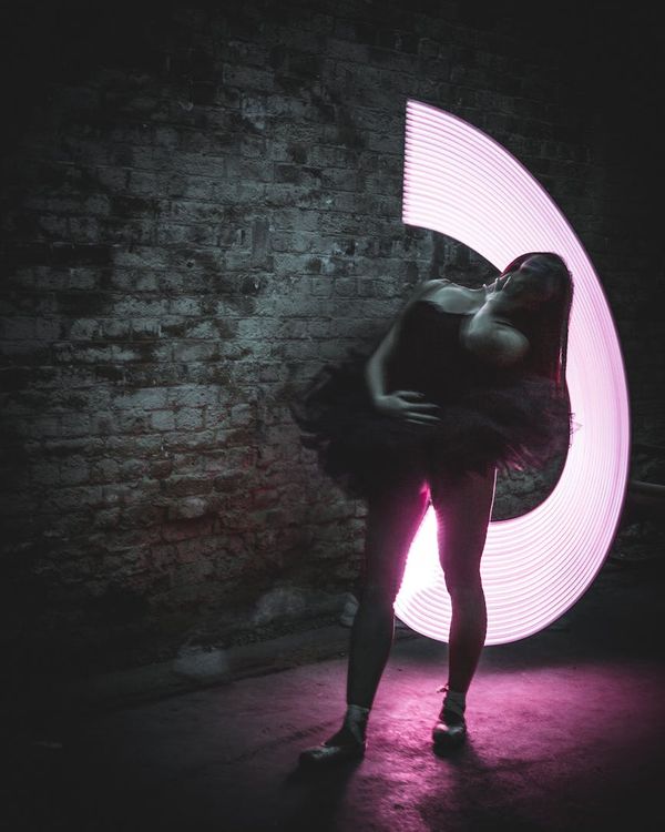 Woman in a dynamic, fluid pose against a dark background with pink light trails.